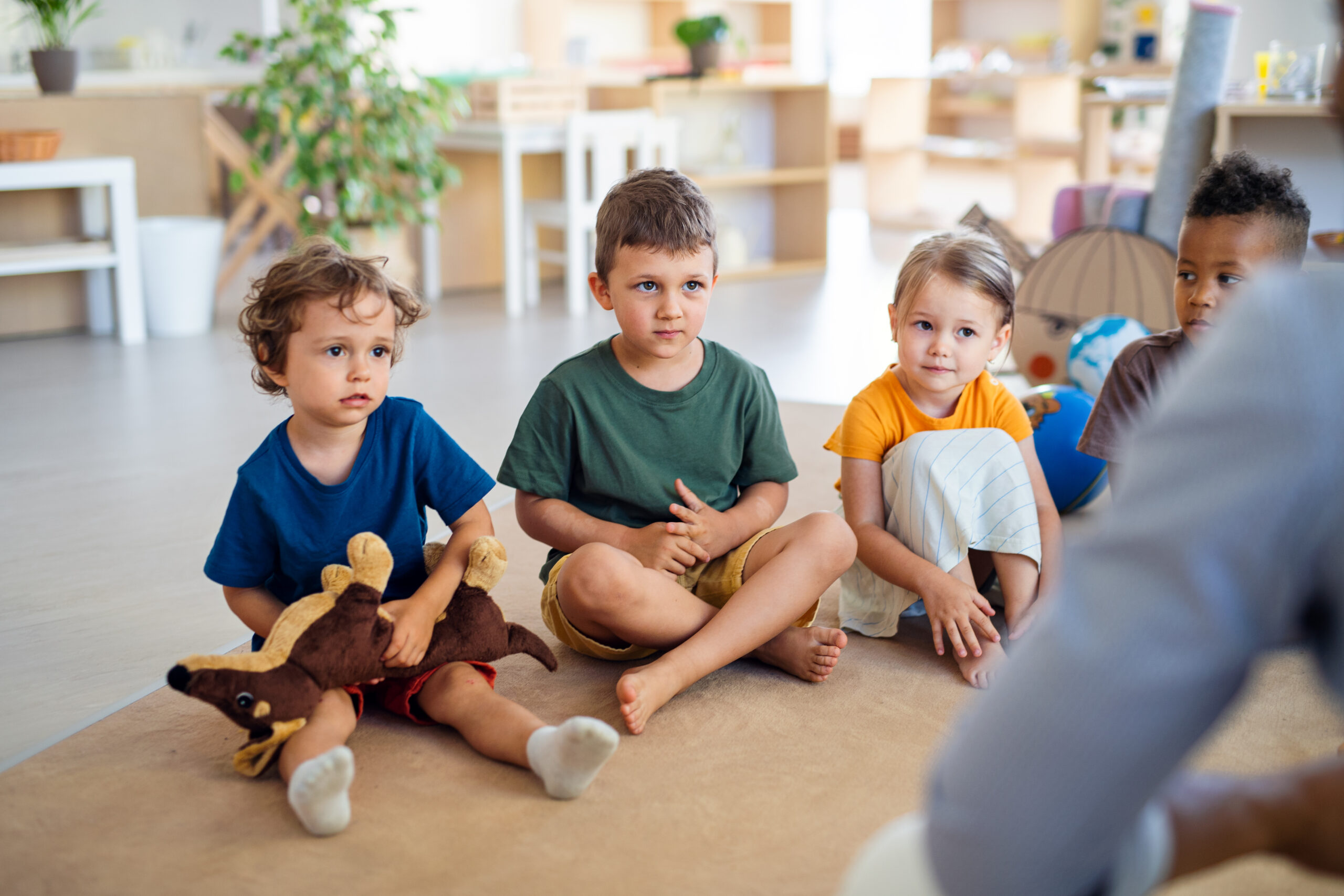 Group of small nursery school children sitting on floor indoors in classroom.
