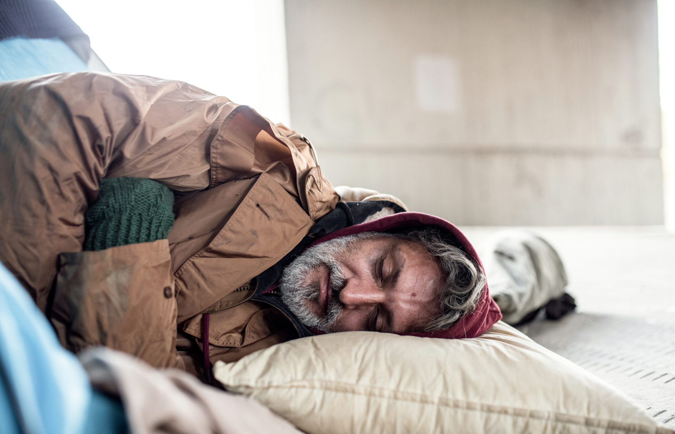 Homeless beggar man lying on the ground outdoors in city, sleeping.