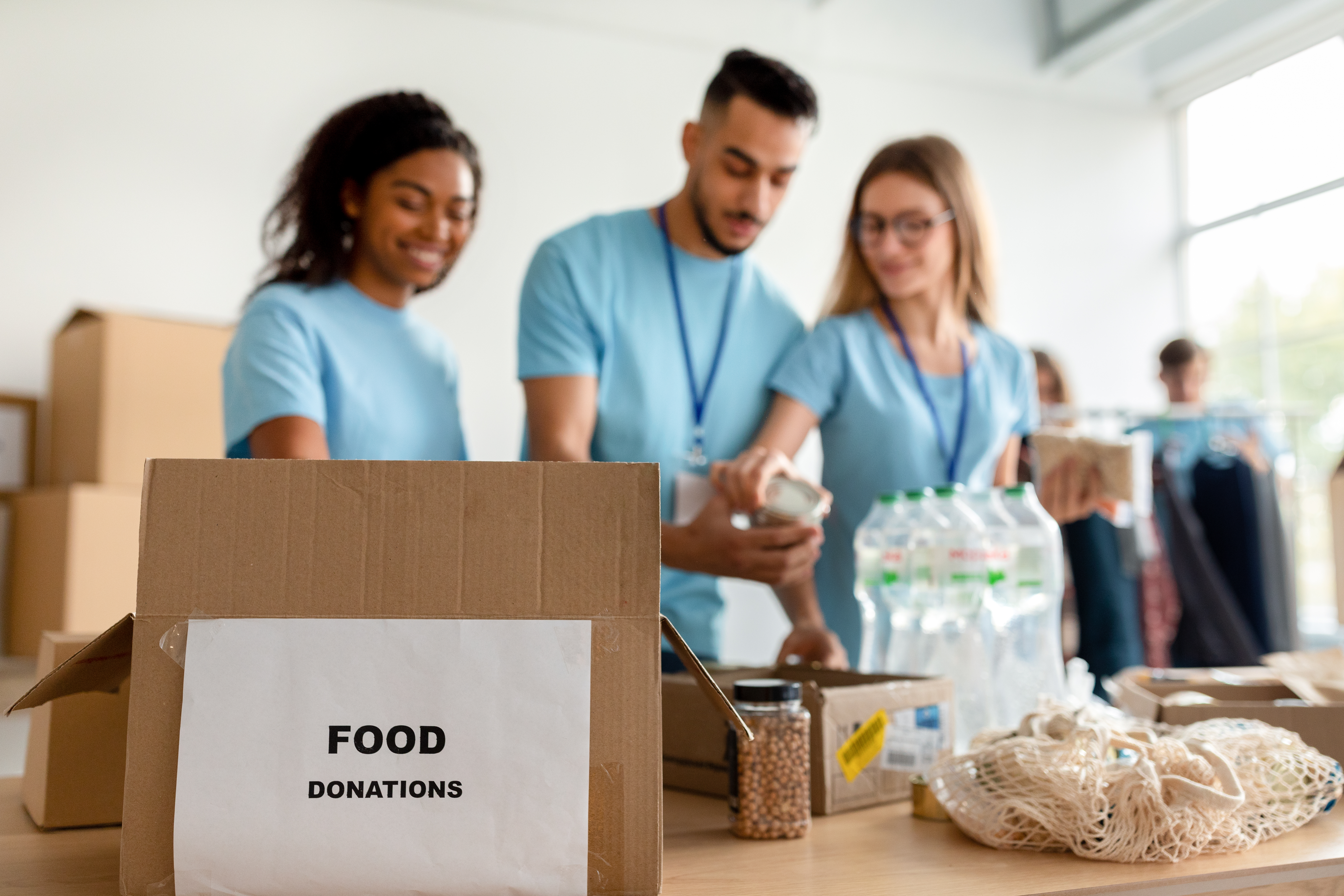 Focus on food donation box. Diverse volunteers sorting and packing prosucts in cardboard boxes
