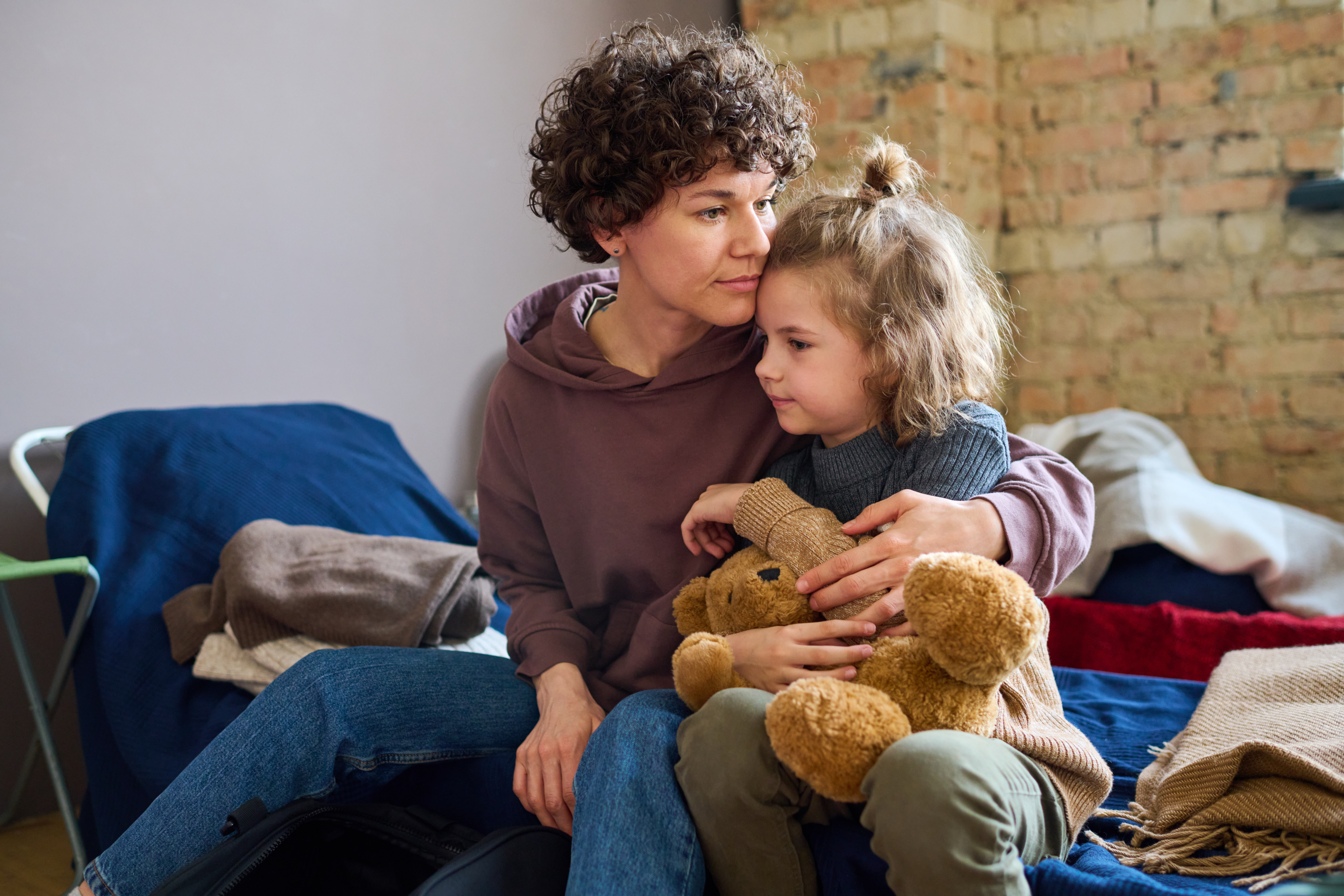 Young woman giving hug to her cute little son with brown soft teddybear