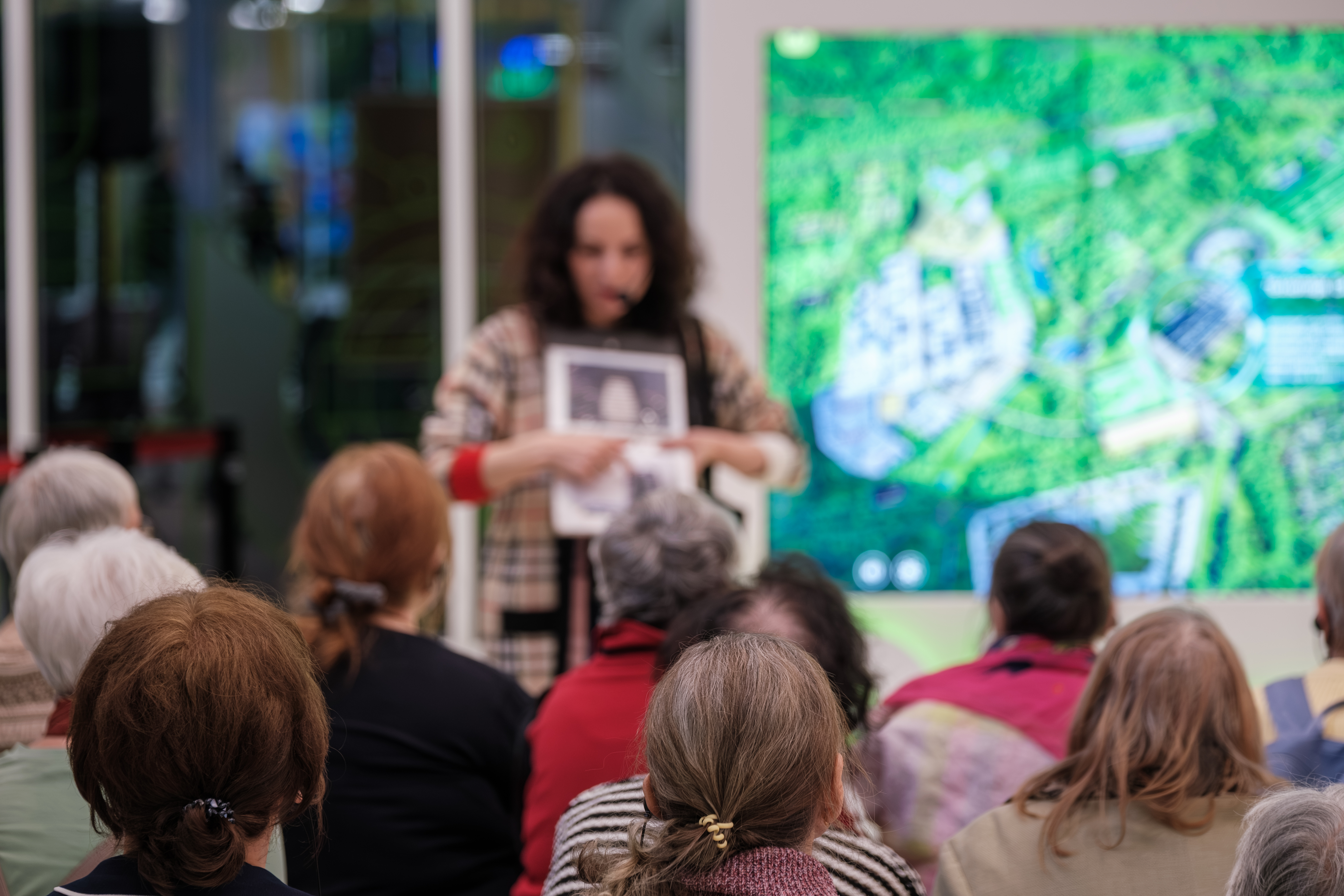 Older adults attend community presentation as woman presenter points to display during educational talk